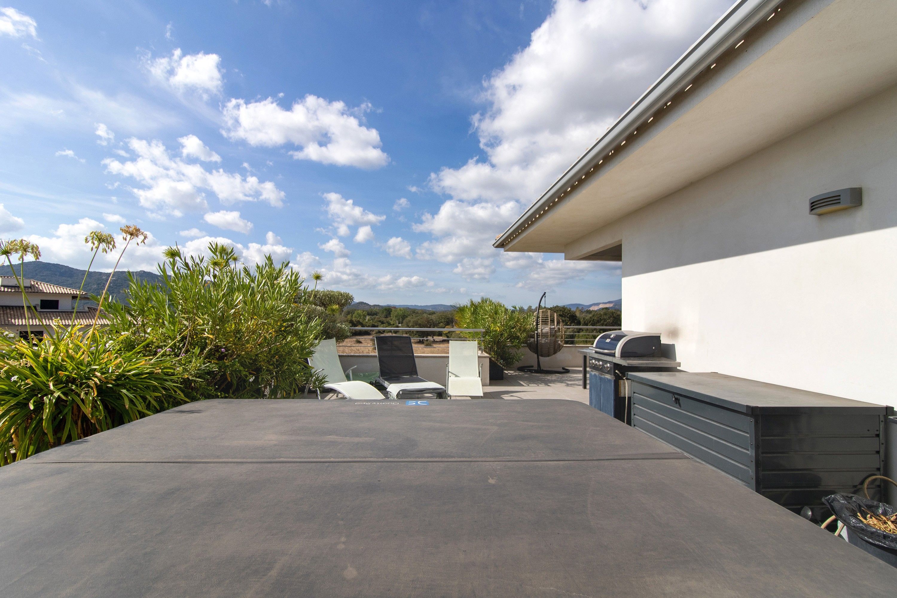 Una terraza en la azotea con una parrilla, mobiliario exterior y vistas del paisaje circundante.