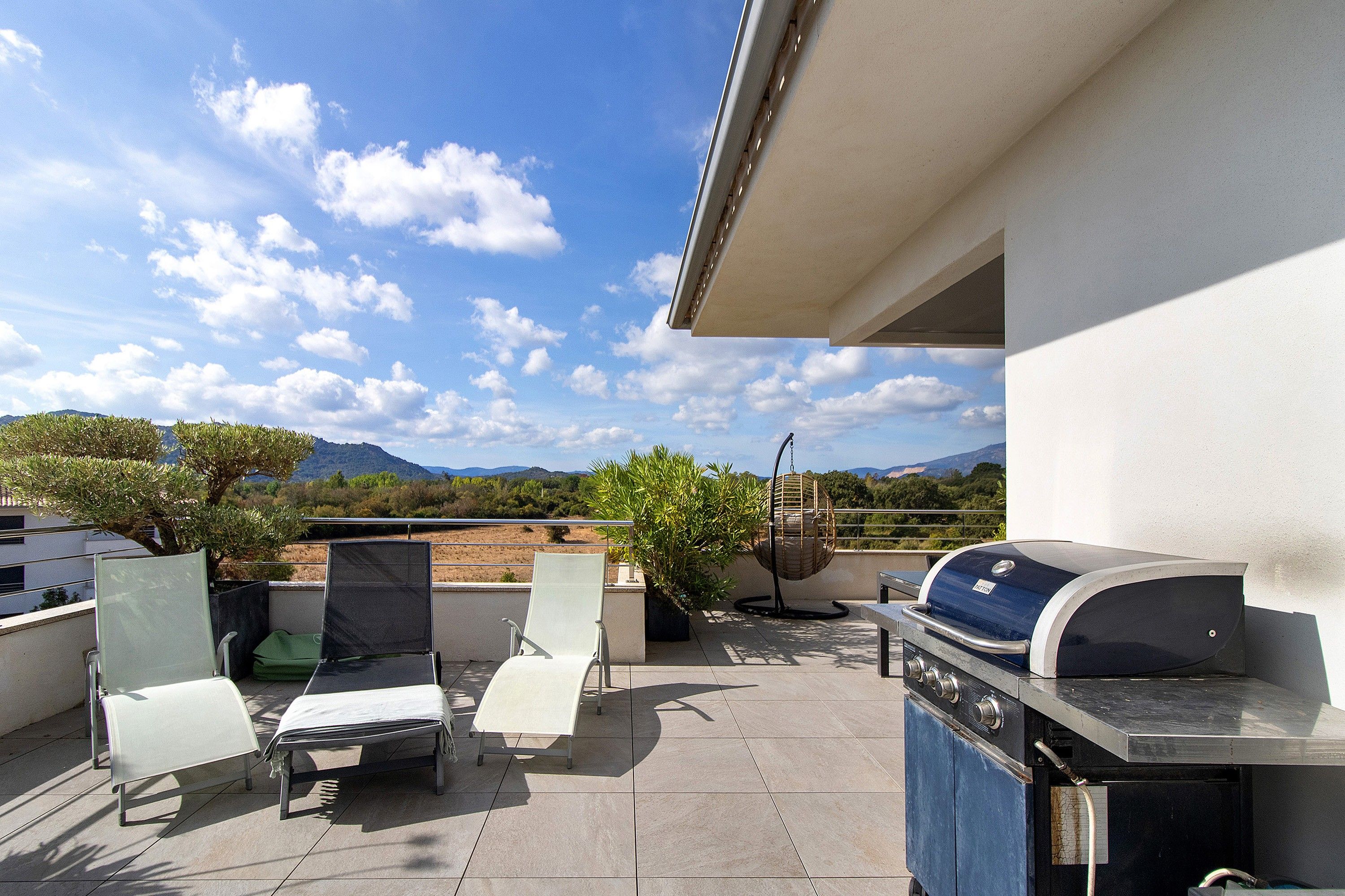 Une terrasse sur le toit équipée d’un barbecue, de deux chaises longues et d’un fauteuil suspendu.