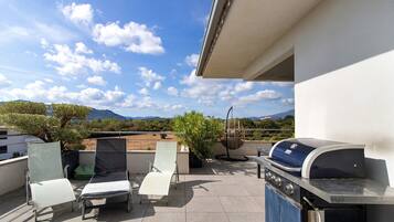 Une terrasse sur le toit équipée d’un barbecue, de deux chaises longues et d’un fauteuil suspendu.