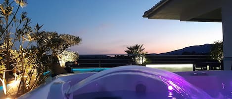 A hot tub with a view of a pool and mountains in the background.