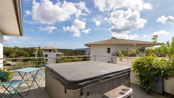 Une terrasse sur le toit dotée d’un jacuzzi, de mobilier d’extérieur et offrant une vue sur les bâtiments et les collines environnants.