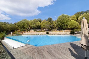 A rectangular swimming pool with a wooden deck surrounding it, set against a backdrop of trees and a stone wall. - Apartment for 4/6, 72 m² Terrace with Private Spa, Pool (Porto-Vecchio)