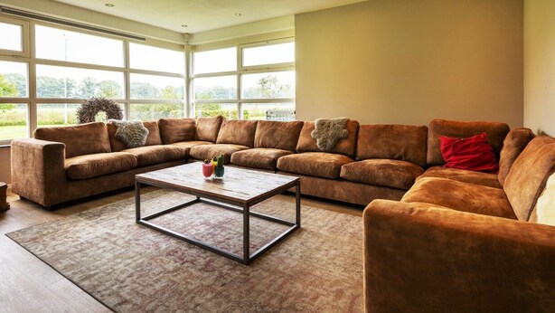 A living room with a sectional sofa, a coffee table, and large windows. - Achterhoek Villa With Heated Pool (Aalten)