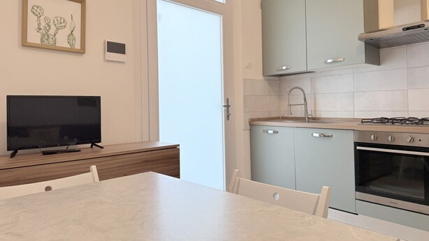Une cuisine moderne avec des meubles de couleur bleu clair, une cuisinière à gaz, un four et un téléviseur posé sur une table en bois.