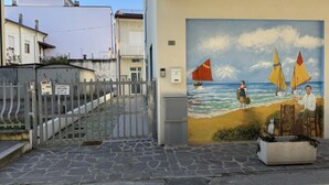 Une rue côtière ornée d’une fresque représentant des voiliers, avec une porte et un bâtiment portant un numéro.