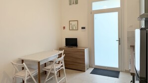 Une petite pièce propre, avec un bureau en bois, une chaise, un téléviseur, une porte et un réfrigérateur.
