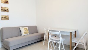 Une pièce moderne avec un canapé gris, une table blanche et deux chaises blanches.