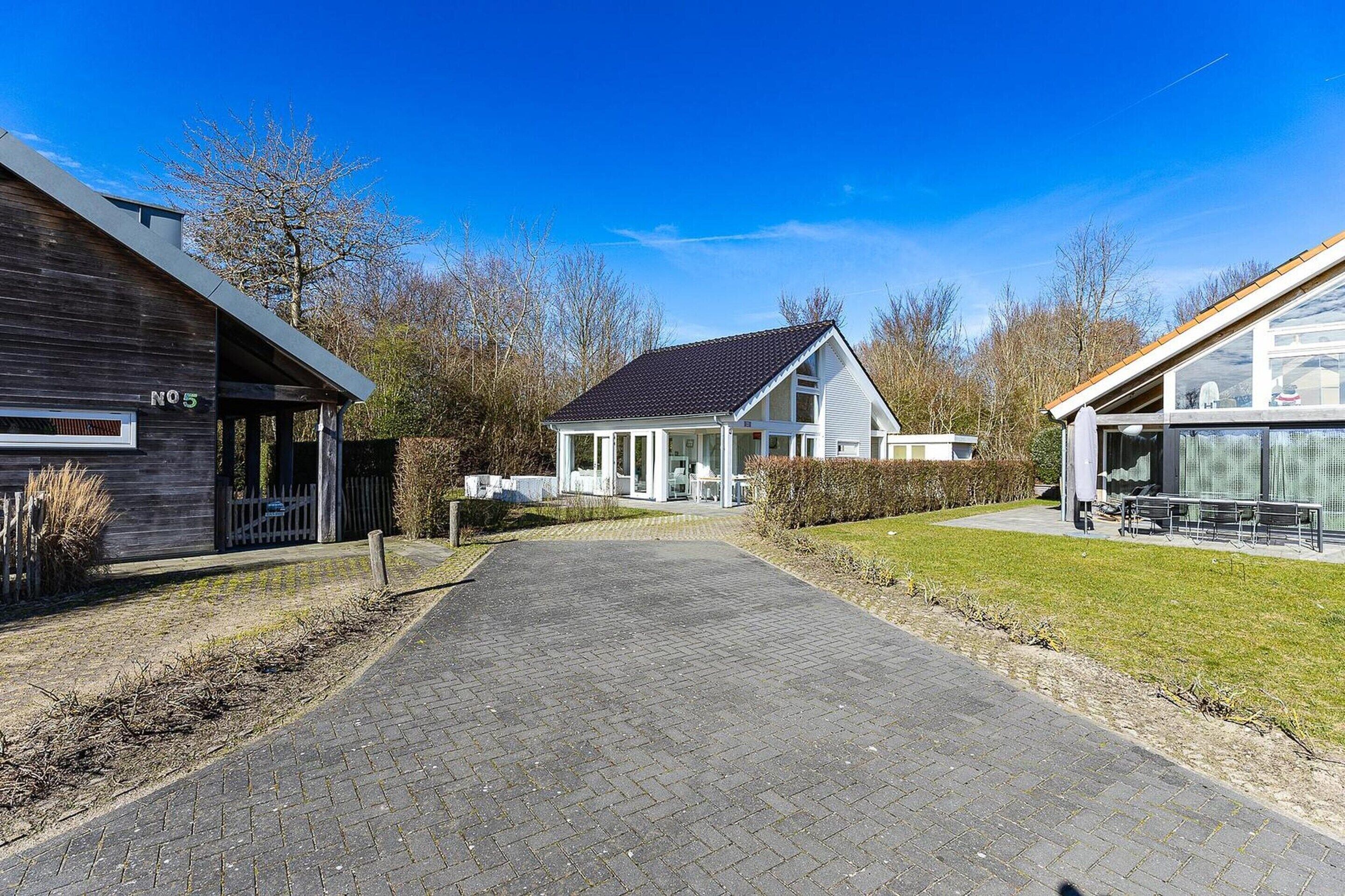 A pathway leading to a modern house with a dark exterior and a white interior, surrounded by a well-maintained lawn and trees.