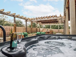 Ein Whirlpool mit einer Holzpergola und Gartenmöbeln im Hintergrund.