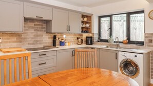 A kitchen with a wooden table, a washing machine, and a window with a view. - Lower Moorwood (Newton Abbot)