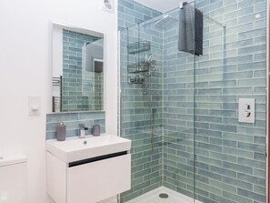 Ein Badezimmer mit Duschkabine aus Glas, einem weißen Waschbecken und einem Spiegel.
