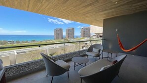 A balcony with modern furniture, a hammock, and a view of the ocean and buildings. - 1-bedroom suite at Solaz, A Luxury Collection Resort, Los Cabos (San José del Cabo)