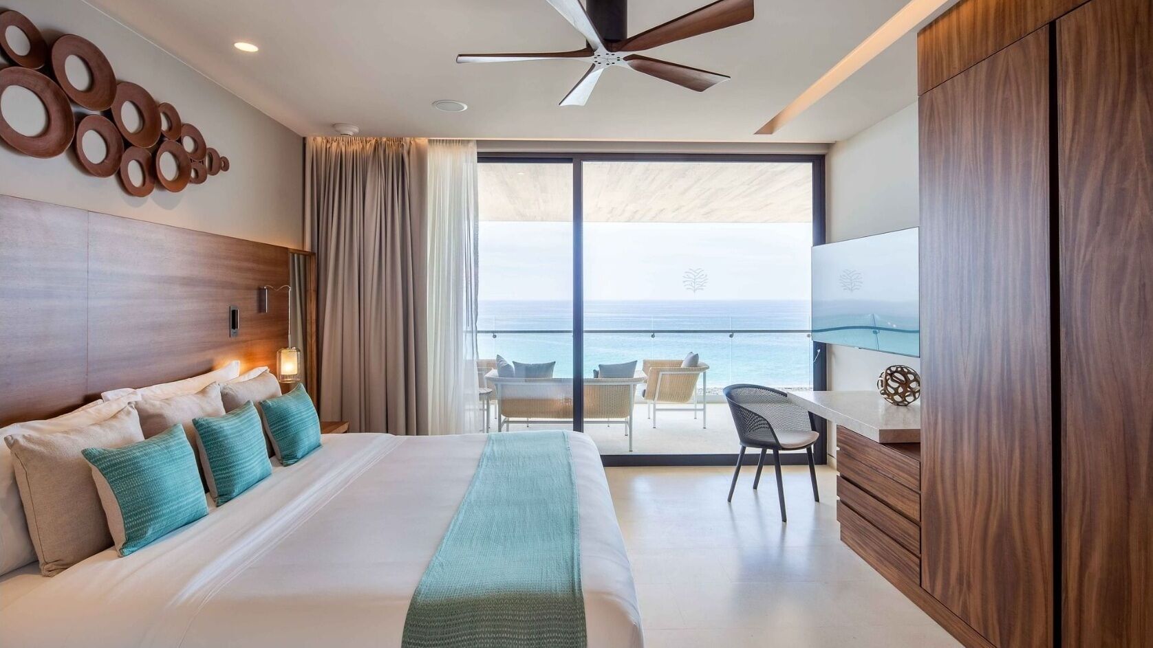 Une chambre d’hôtel équipée d’un lit, d’un bureau, d’une chaise, d’un ventilateur de plafond et offrant une vue sur l’océan.