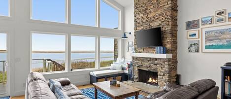 A spacious living room with a stone fireplace, large windows, and a view of the outdoors.