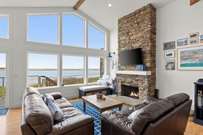 A spacious living room with a stone fireplace, large windows, and a view of the outdoors.