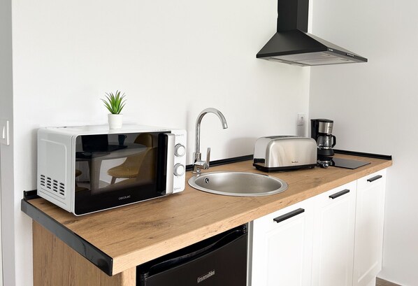 A compact kitchen with a microwave, toaster, sink, and a coffee maker.
