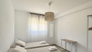 A bedroom with two beds, a desk, a hanging light fixture, and a window with curtains. - Apartamentos El Camino Resorts (Cóbreces)