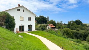 A white house with a paved path leading to the entrance, surrounded by greenery and hills. - Apartamentos El Camino Resorts (Cóbreces)