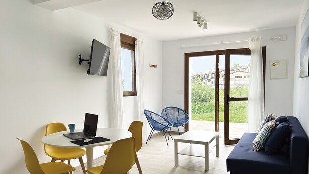 A modern living room with a dining area, a sofa, and a TV mounted on the wall. - Apartamentos El Camino Resorts (Cóbreces)