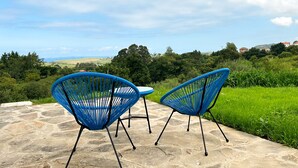 Two blue chairs on a stone patio with a view of a green landscape and distant buildings. - Apartamentos El Camino Resorts (Cóbreces)
