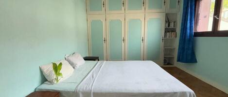 Un dormitorio con cama, suelo de madera, un armario y una ventana con cortinas.