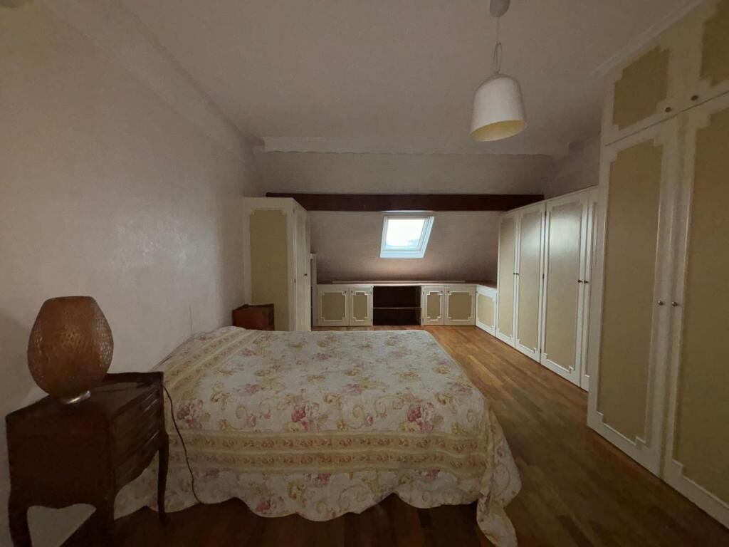A bedroom with a bed, a desk, a lamp, a wardrobe, and a skylight.