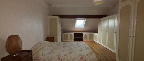 A bedroom with a bed, a desk, a lamp, a wardrobe, and a skylight.