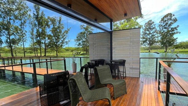 A wooden deck with outdoor furniture, a brick wall, and a view of a lake and trees.
