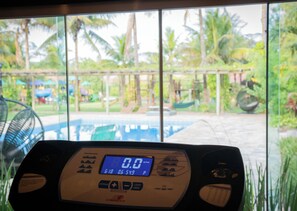 A treadmill with a digital display, a window view of a pool and greenery. - Sitio Castelinho Hotel Fazenda (Cesário Lange)
