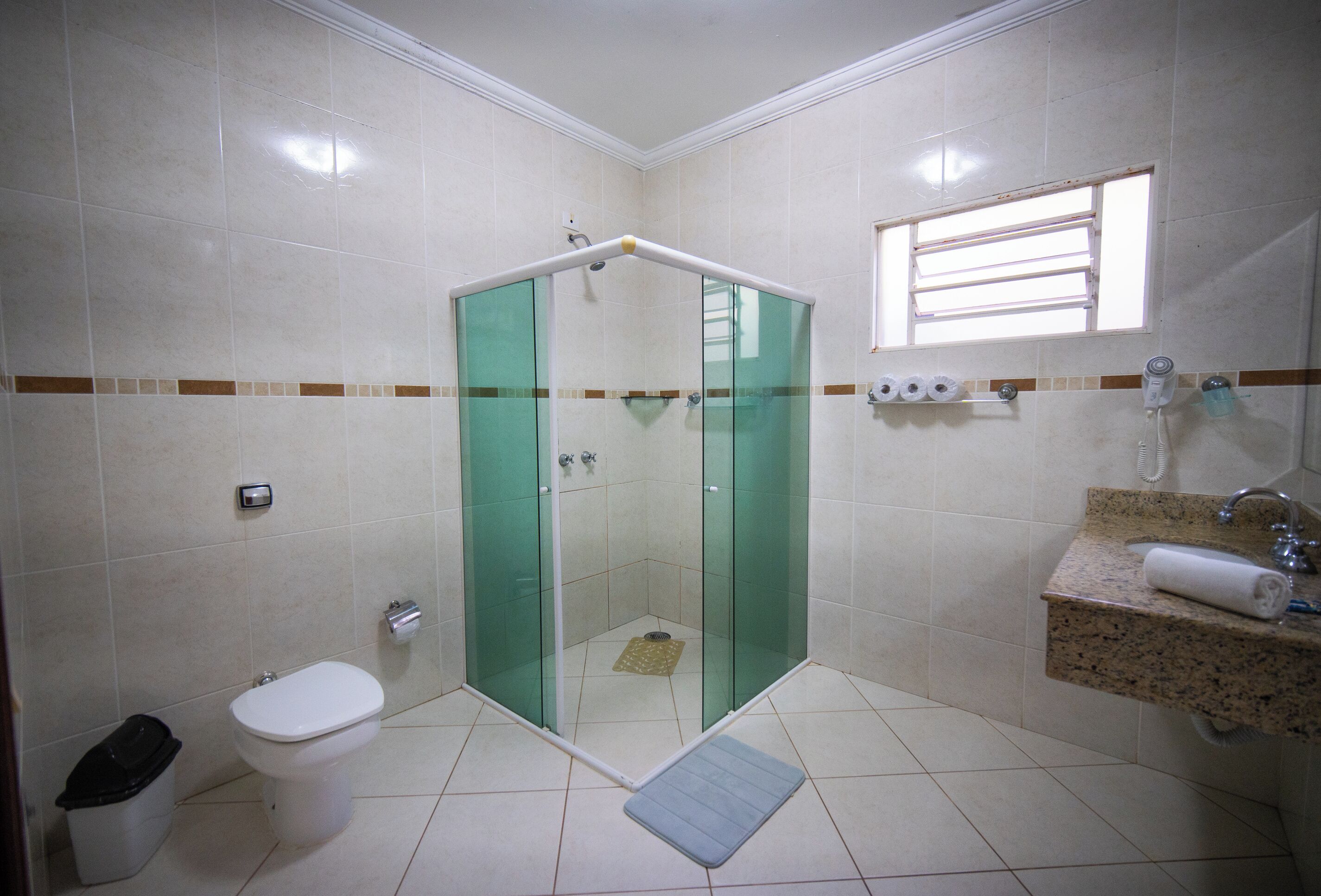 A bathroom with a glass-enclosed shower, a toilet, a trash bin, and a sink with a towel.