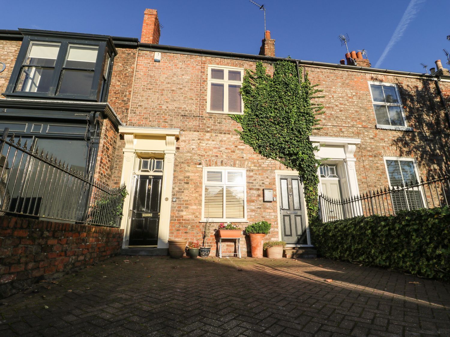 A brick house with a black door, white shutters, and a small garden with potted plants.