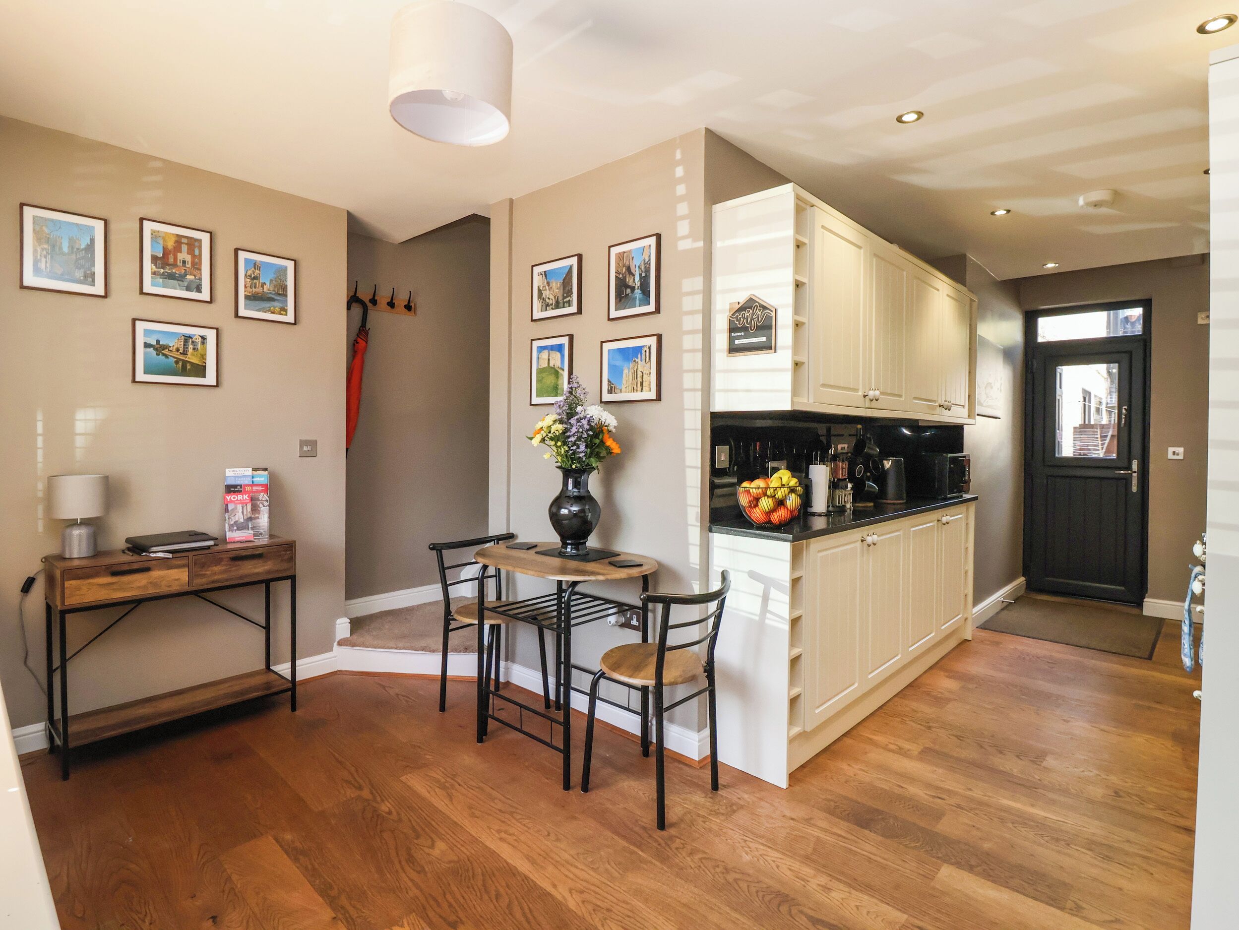 A compact kitchen with wooden cabinets, a dining area with a table and chairs, and a hallway with a door.