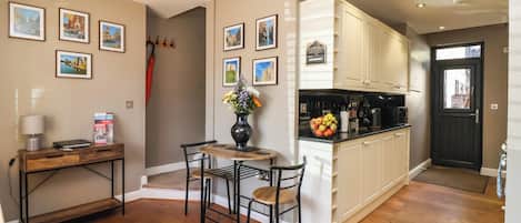 A compact kitchen with wooden cabinets, a dining area with a table and chairs, and a hallway with a door.