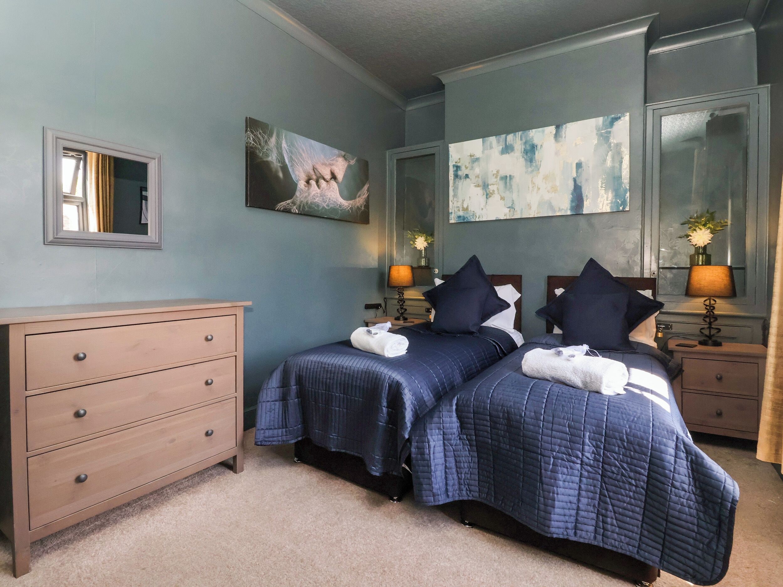 A hotel room with two beds, a dresser, and artwork on the walls.