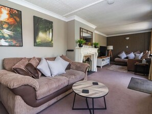 En stue med en brun sofa, et rundt sofabord, en pejs og et fjernsyn.