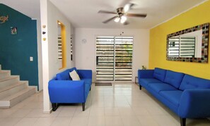 A living room with two blue sofas, a ceiling fan, a clock, and a window with blinds. - Casa Diamante : 4 Bedrooms + Private Swimming Pool and 2 Premium Suites (Mérida)