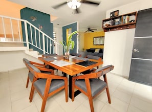 Un coin repas avec une table et des chaises en bois, un ventilateur de plafond et un escalier doté d’une rampe.