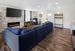 A living room with a sectional sofa, a flat-screen TV, a fireplace, and a coat rack.