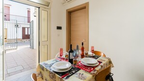 A dining table set with plates, glasses, and bottles, with a door and a view of a building outside. - Holiday Home 'Lu Sule Lu Mare Lu Ientu1' with Private Garden, Wi-Fi and Air Conditioning (Porto Cesareo)
