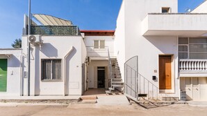A two-story building with a staircase leading to a balcony, a green shuttered door, and a metal fence. - Holiday Home 'Lu Sule Lu Mare Lu Ientu1' with Private Garden, Wi-Fi and Air Conditioning (Porto Cesareo)
