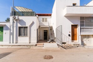 A two-story building with a staircase leading to a balcony, a green shuttered door, and a metal fence. - Holiday Home 'Lu Sule Lu Mare Lu Ientu1' with Private Garden, Wi-Fi and Air Conditioning (Porto Cesareo)