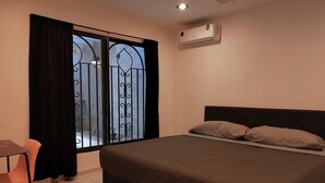 A bedroom with a bed, a window with curtains, a small table, and an air conditioning unit.
