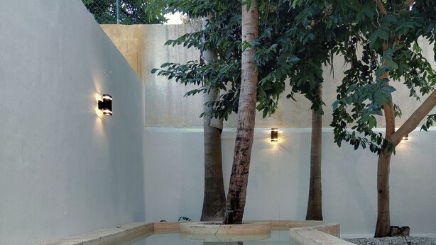 A swimming pool with a clear blue water surface, surrounded by white walls and trees.