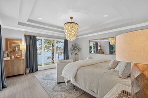 A bedroom with a bed, a dresser, a mirror, a chandelier, and a view of the outdoors.
