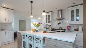 A modern kitchen with white cabinetry, a central island with bar stools, pendant lighting, and a stainless steel range hood. - Luxurious 3BDR 3BATH Hounslow by the Airport (Greater London)