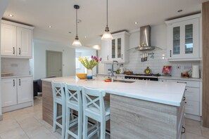 A modern kitchen with white cabinetry, a central island with bar stools, pendant lighting, and a stainless steel range hood. - Luxurious 3BDR 3BATH Hounslow by the Airport (Greater London)