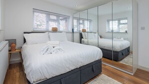 A modern bedroom with a large bed, a mirror, and a window with blinds. - Luxurious 3BDR 3BATH Hounslow by the Airport (Greater London)