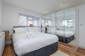 A modern bedroom with a large bed, a mirror, and a window with blinds. - Luxurious 3BDR 3BATH Hounslow by the Airport (Greater London)