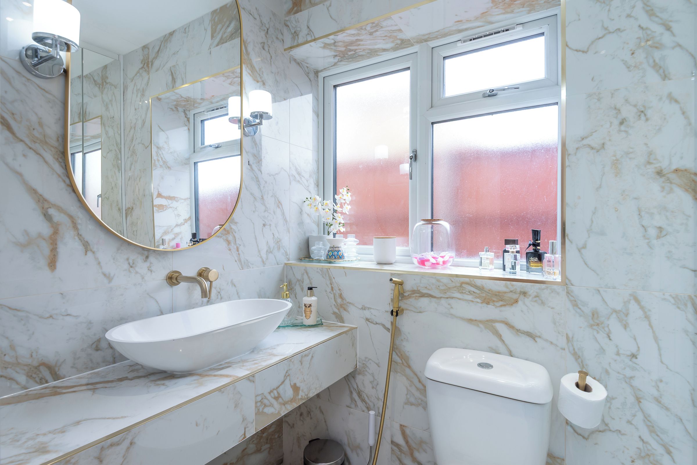 Et badeværelse med en hvid vask, toilet, bidet, et vindue og et spejl.