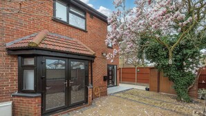 A brick house with a conservatory, a garden with a tree bearing pink flowers, and a paved driveway. - Luxurious 3BDR 3BATH Hounslow by the Airport (Greater London)